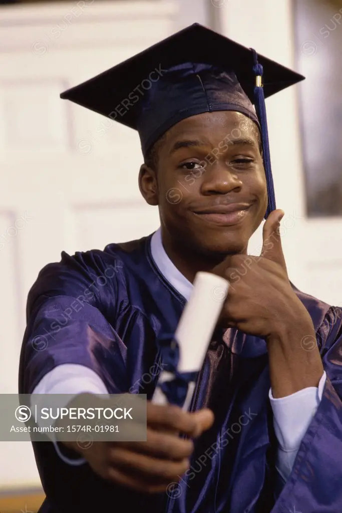 Portrait of a teenage boy showing a thumbs up sign with a graduation degree in hand