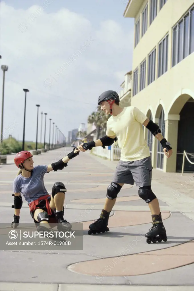 Young man helping up a young woman on inline skates