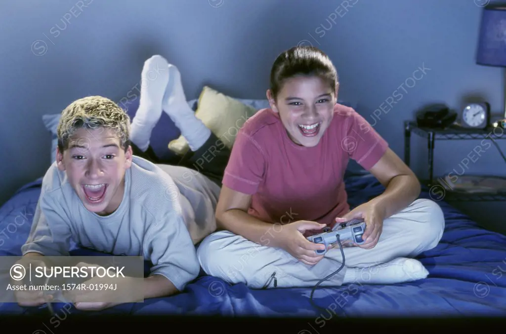 Teenage boy and girl sitting on the bed and playing a video game