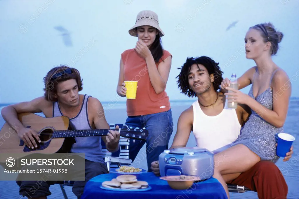 Two young couples sitting with a guitar on the beach