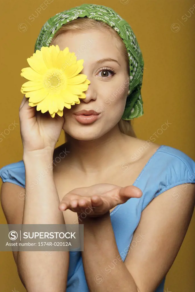 Portrait of a young woman holding a flower in front of her eye