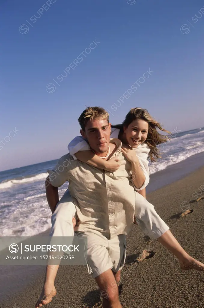 Young woman riding piggyback on a young man at the beach
