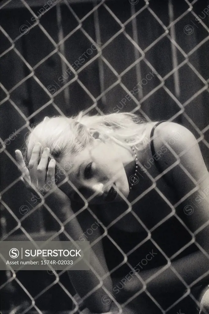 Teenage girl sitting behind a chain-link fence