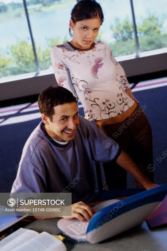 Portrait of teenage boy in front of a laptop with a teenage girl behind him