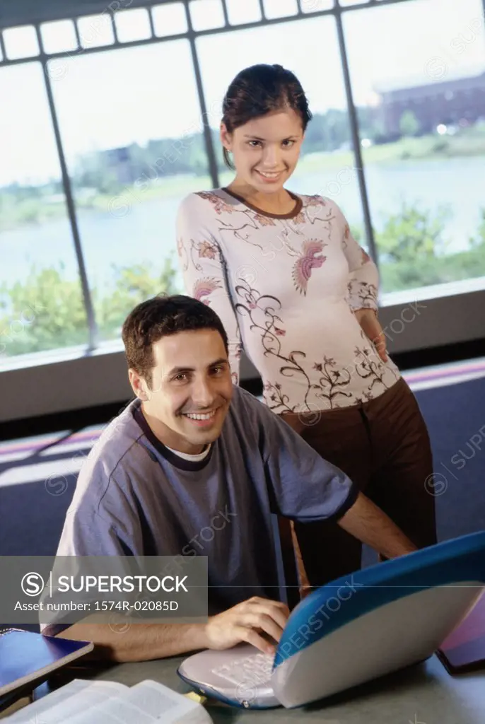 Portrait of a teenage boy sitting in front of a laptop with a teenage girl standing behind him