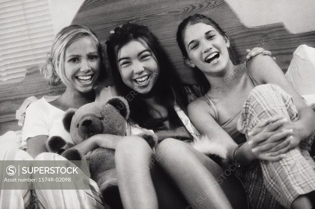 Portrait of three teenage girls sitting on a bed at a slumber party