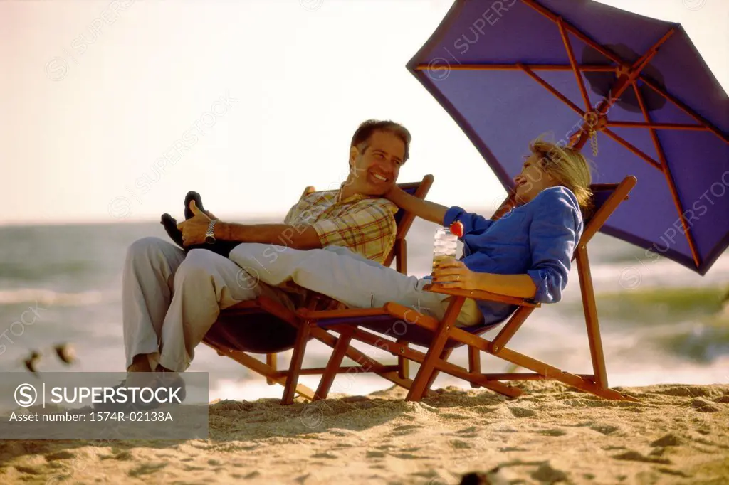 Mid adult couple sitting on lounge chairs on the beach