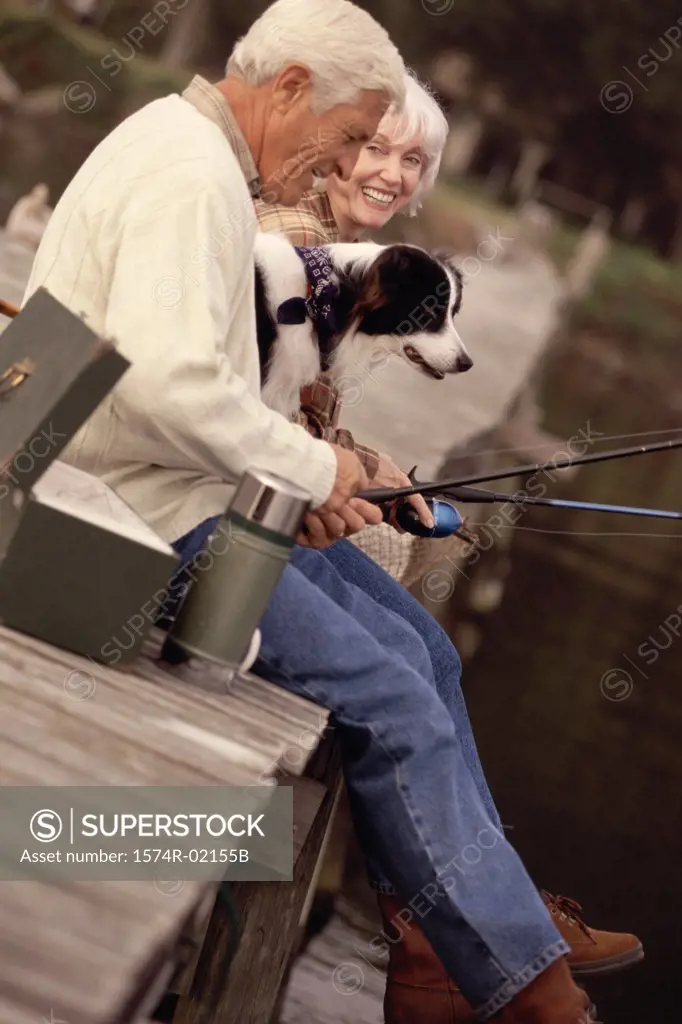 Side profile of a senior couple fishing on a pier with their dog