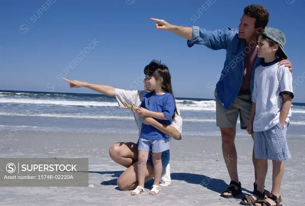 Young couple pointing on the beach with their son and daughter