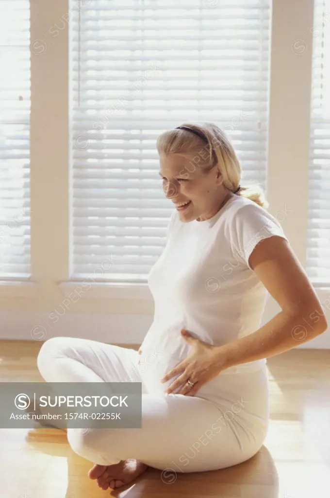 Pregnant woman sitting on the floor touching her abdomen