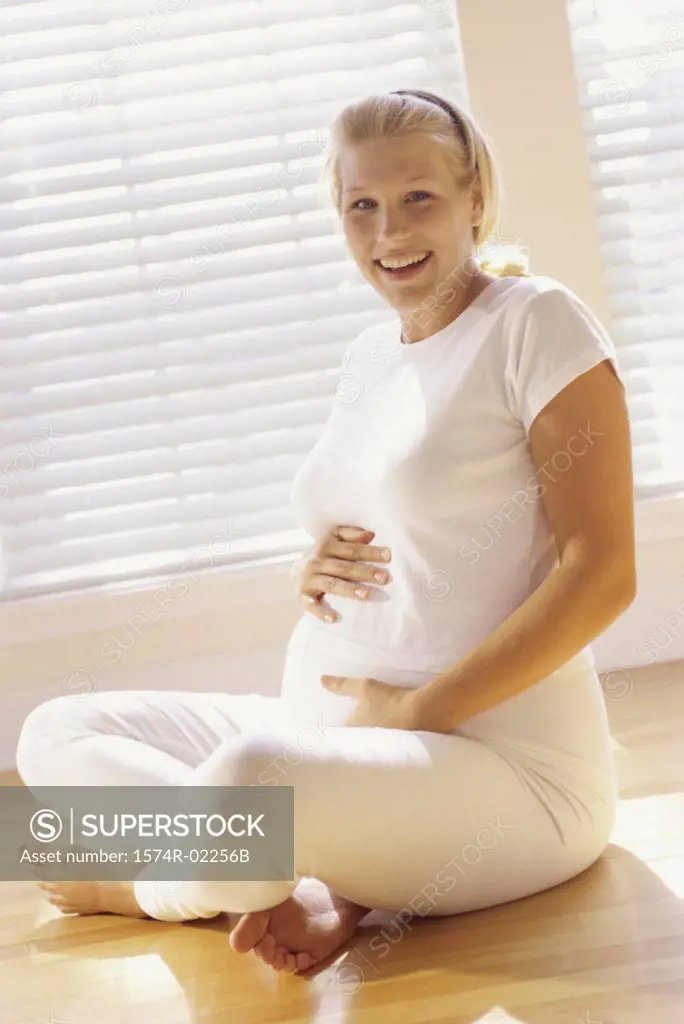 Pregnant woman sitting on the floor touching her abdomen