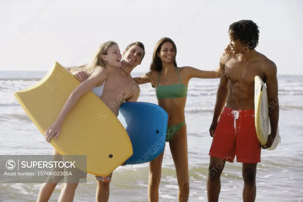 Two teenage couples standing on the beach holding boogie boards