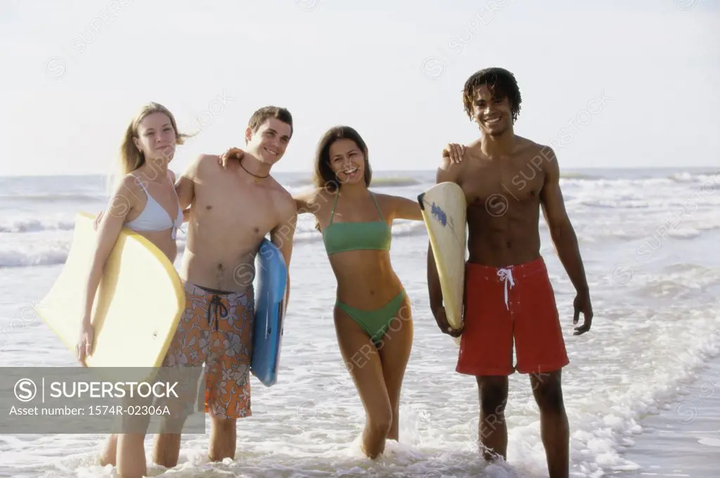 Portrait of two teenage couples standing on the beach holding boogie boards
