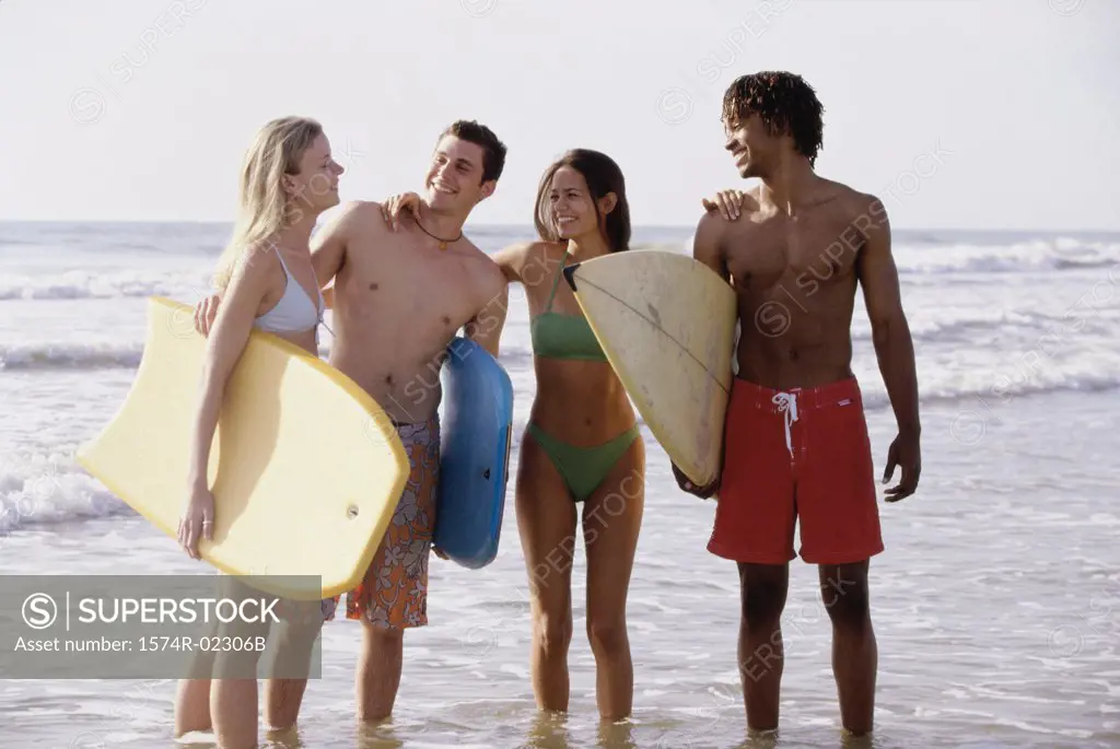 Two teenage couples standing on the beach holding boogie boards