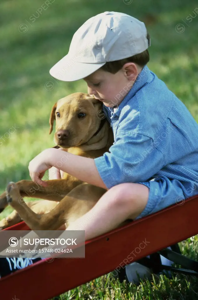 Side profile of a boy sitting in a toy wagon holding his dog