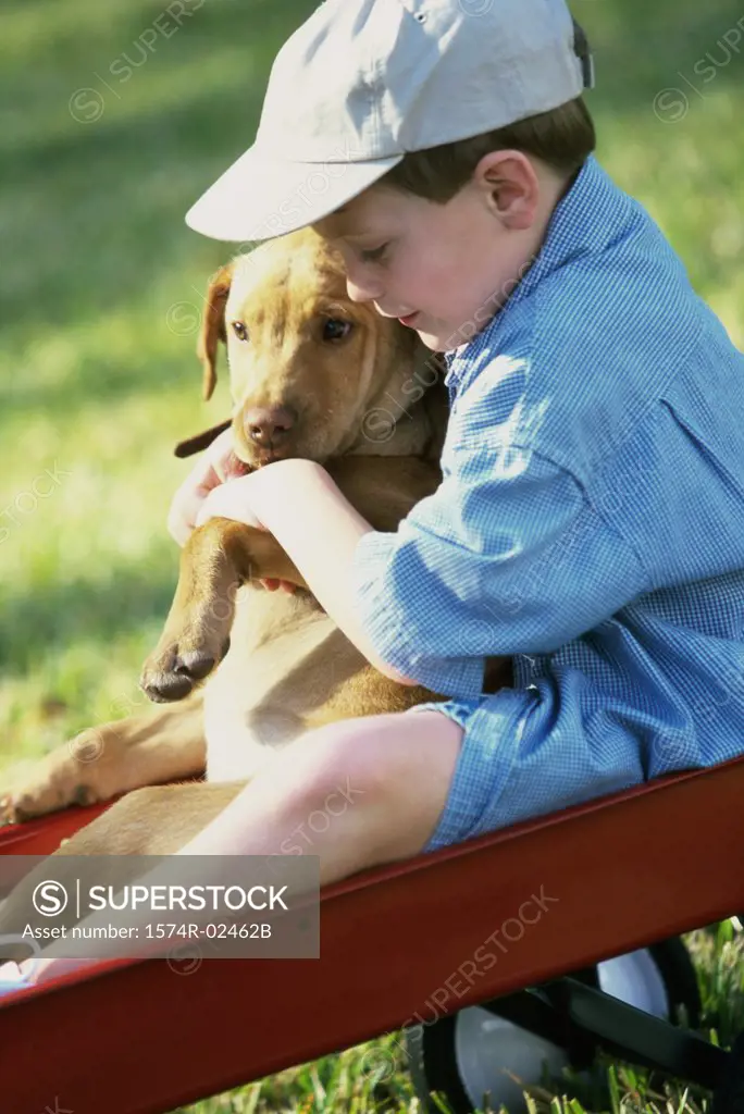 Side profile of a boy sitting in a toy wagon holding his dog