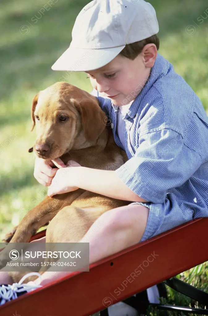 Boy sitting in a toy wagon holding his dog
