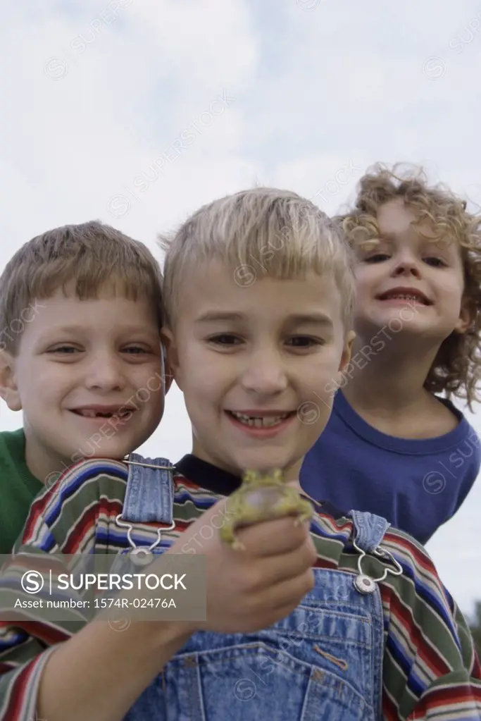 Low angle view of a boy standing with his friends holding a frog