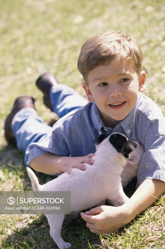 Boy lying on a lawn holding a puppy