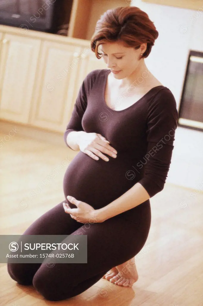 Pregnant woman kneeling on the floor touching her abdomen
