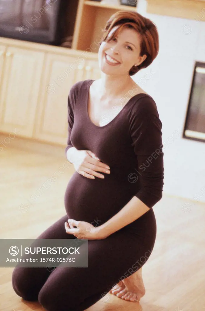 Pregnant woman kneeling on the floor touching her abdomen