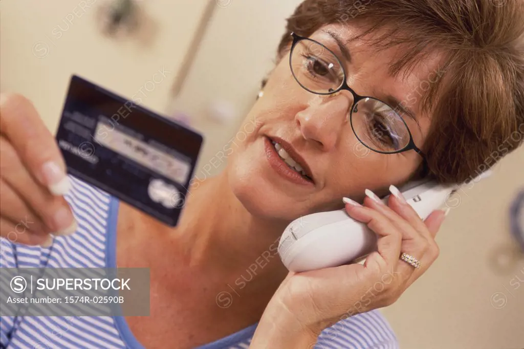 Mid adult woman talking on a cordless phone holding a credit card