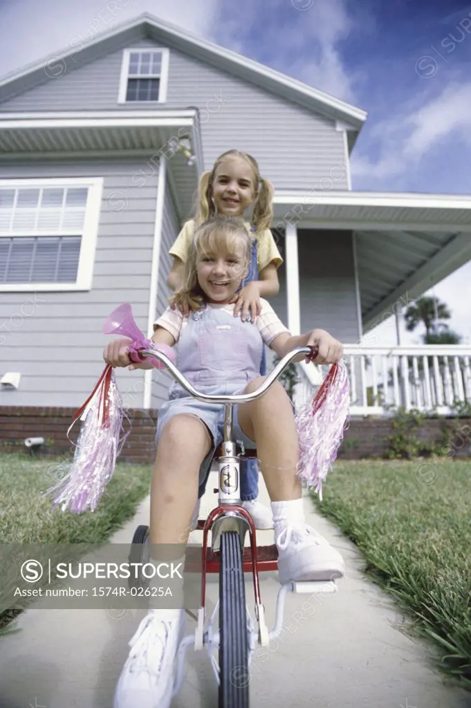 Portrait of two girls riding a tricycle