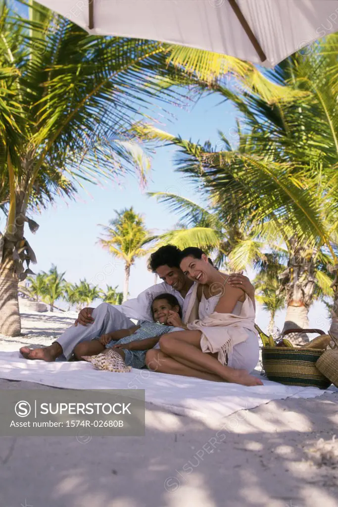 Low angle view of parents sitting with their daughter on the beach