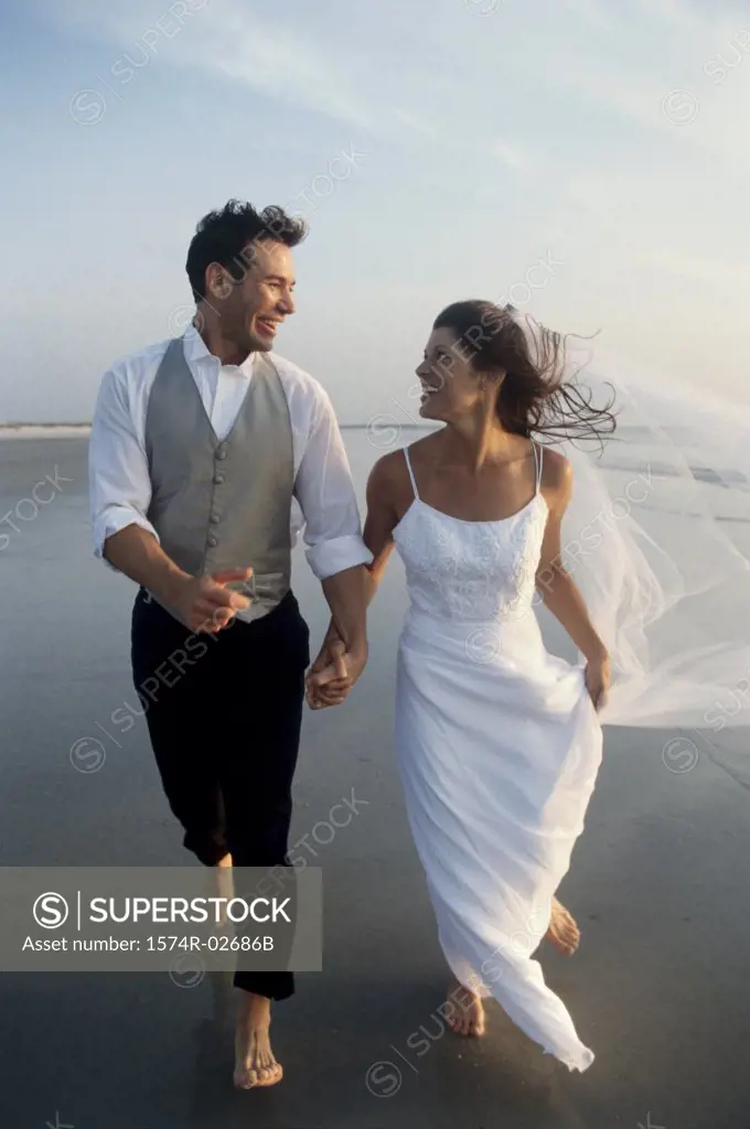 Newlywed couple holding hands running on the beach