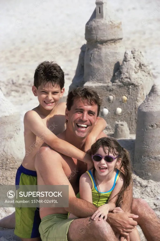 Portrait of a father with his son and daughter sitting on the beach