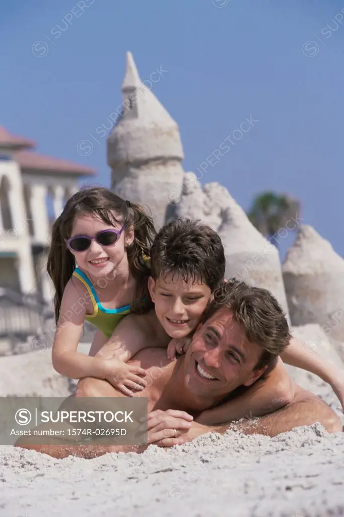 Portrait of a father lying on the beach with his son and daughter