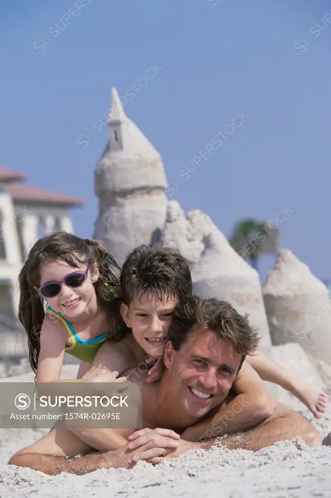 Portrait of a father lying on the beach with his son and daughter