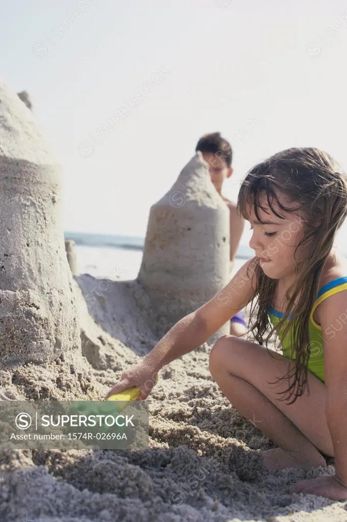 Side profile of a girl and a boy making sand castles on the beach