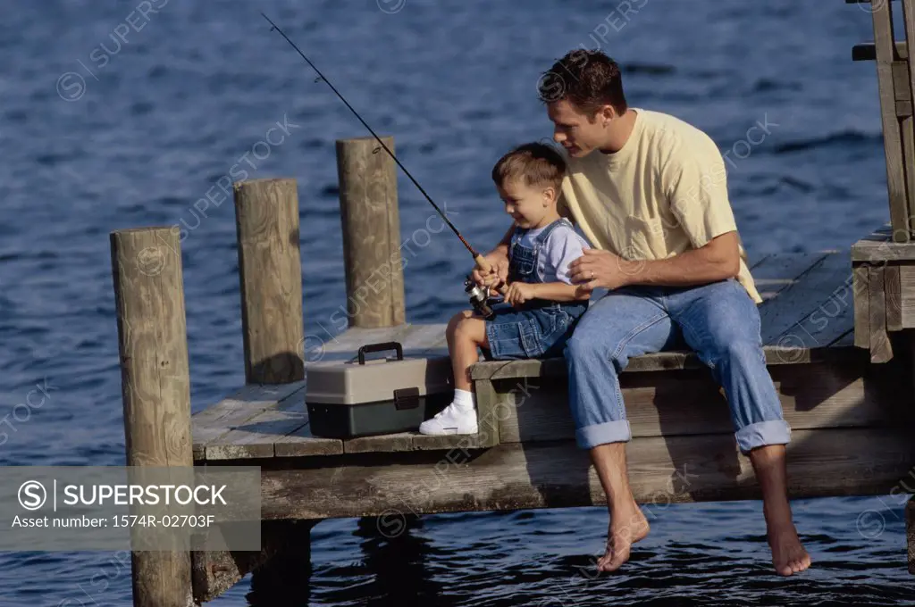 Father and his son sitting on a pier fishing