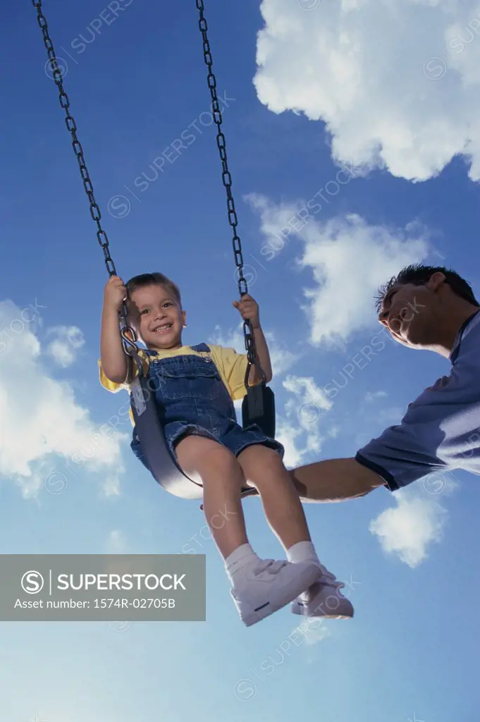 Low angle view of a father pushing his son on a swing
