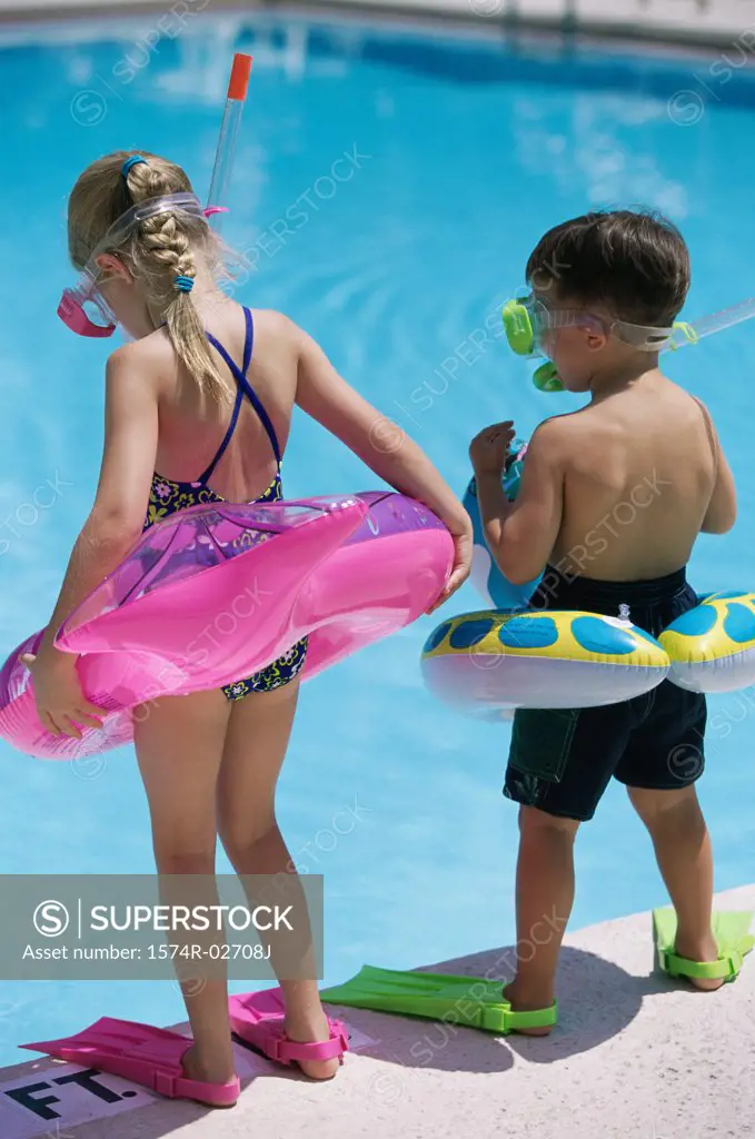 Rear view of a boy and a girl standing at the poolside wearing snorkels and flippers