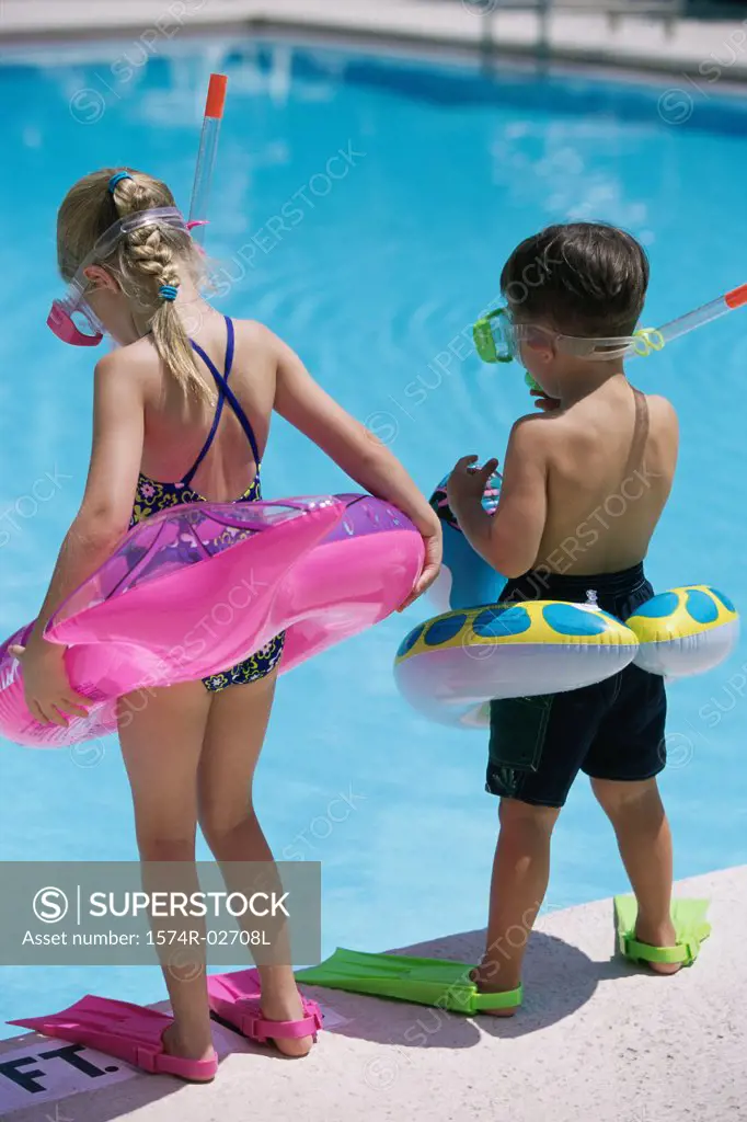 Rear view of a boy and a girl standing at the poolside wearing snorkels and flippers