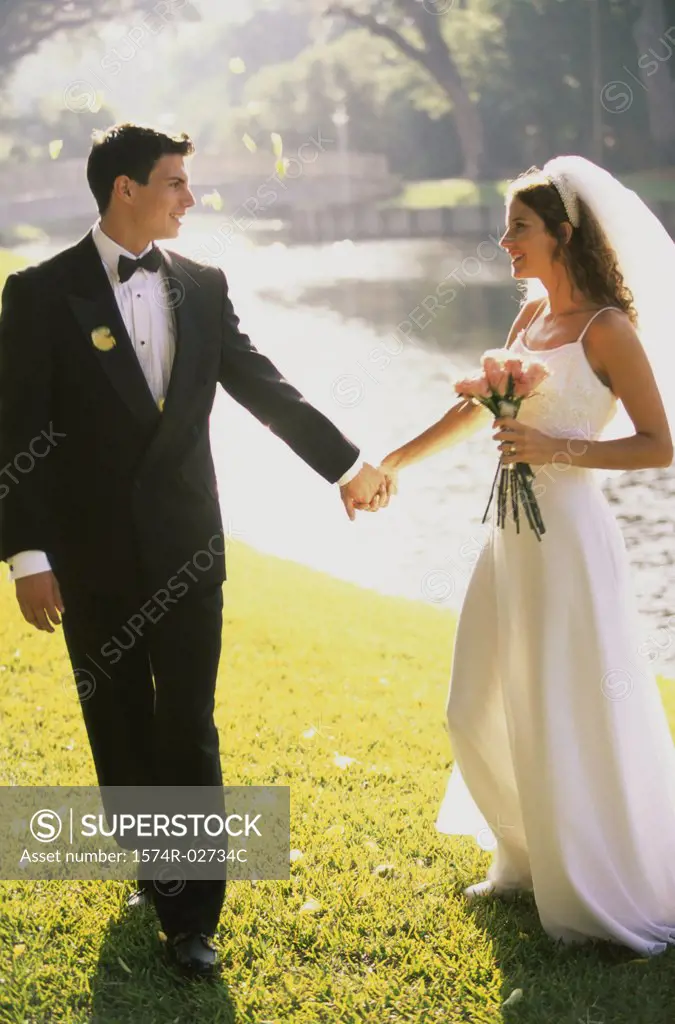 Newlywed couple holding hands and walking by a lake