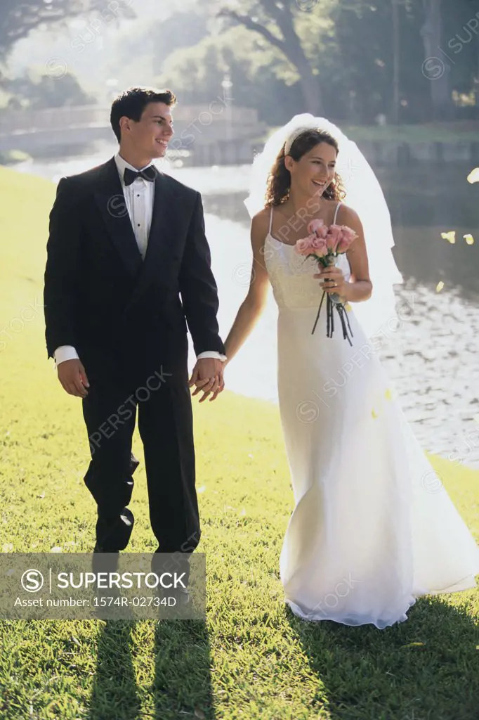 Newlywed couple holding hands and walking by a lake