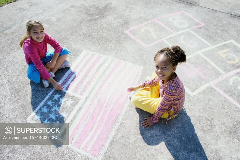 Portrait of two girls drawing on the ground with chalk