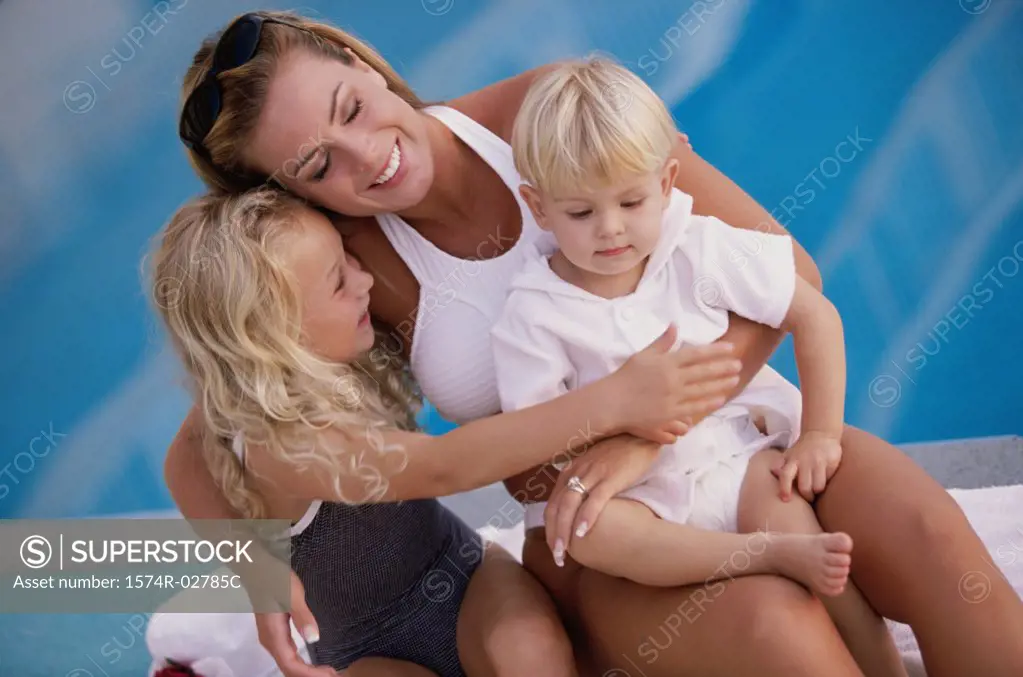 Mother holding her son and daughter beside a swimming pool