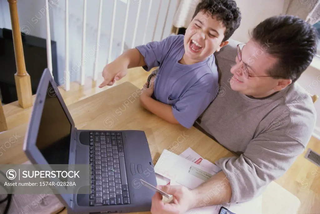 High angle view of a father and his son sitting in front of a laptop holding a credit card