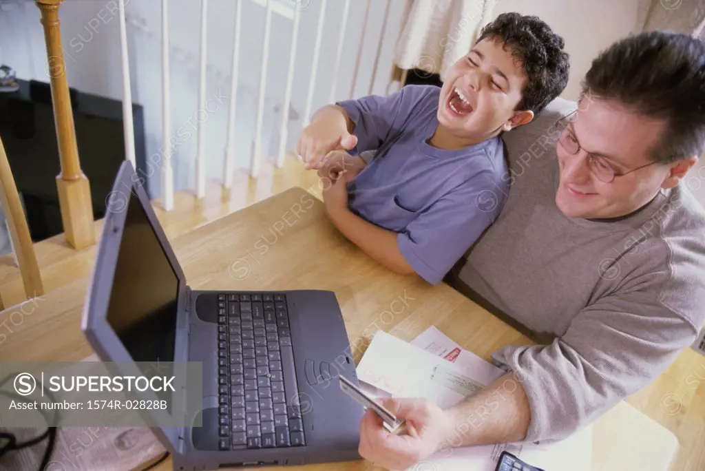 High angle view of a father and his son sitting in front of a laptop holding a credit card