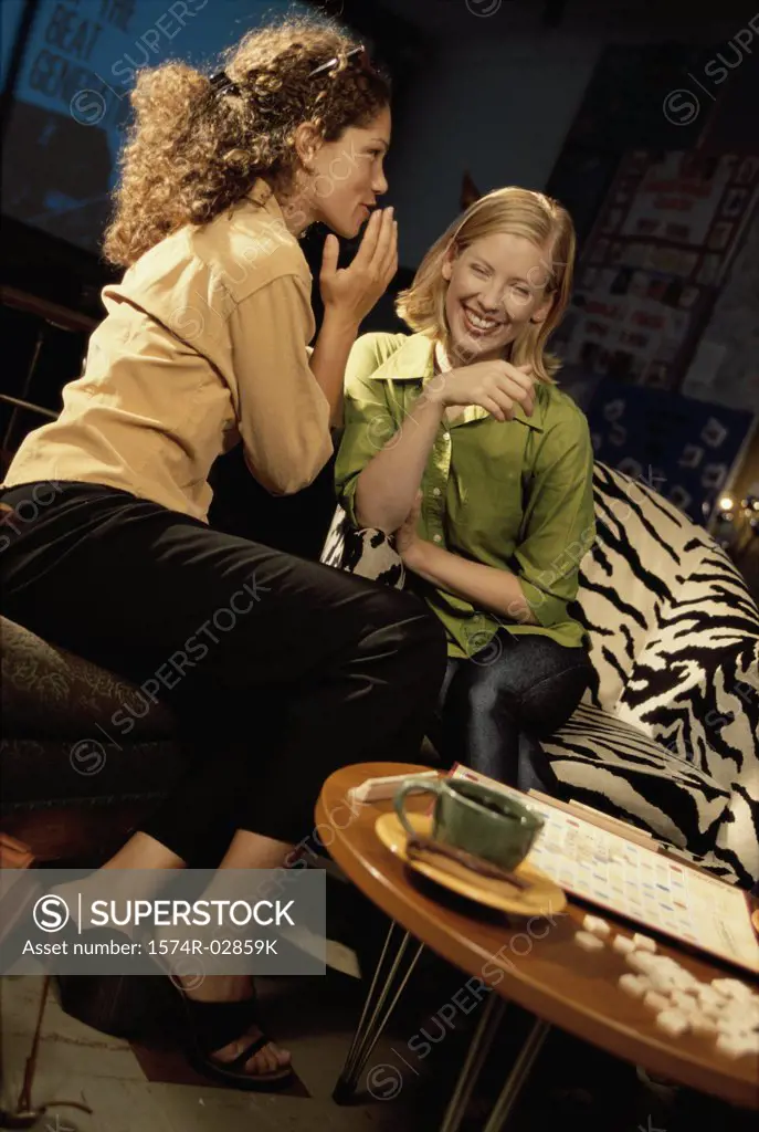 Two young women sitting in a cafeteria whispering
