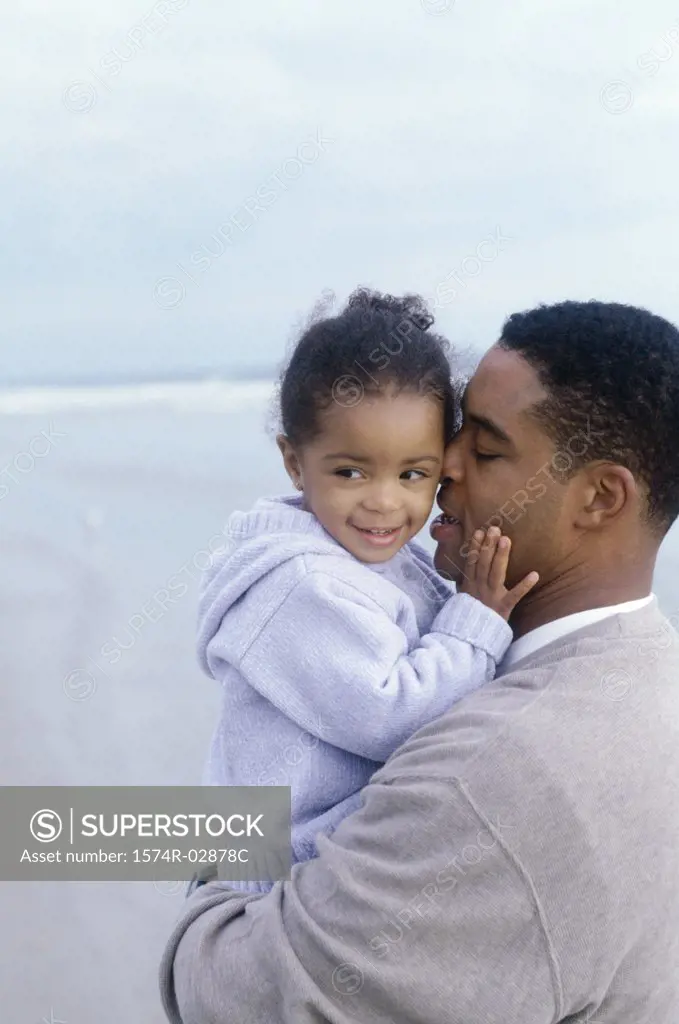 Side profile of a father kissing his daughter on the beach