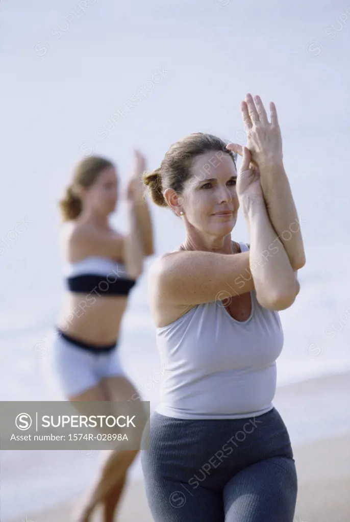 Two mid adult women performing yoga on the beach