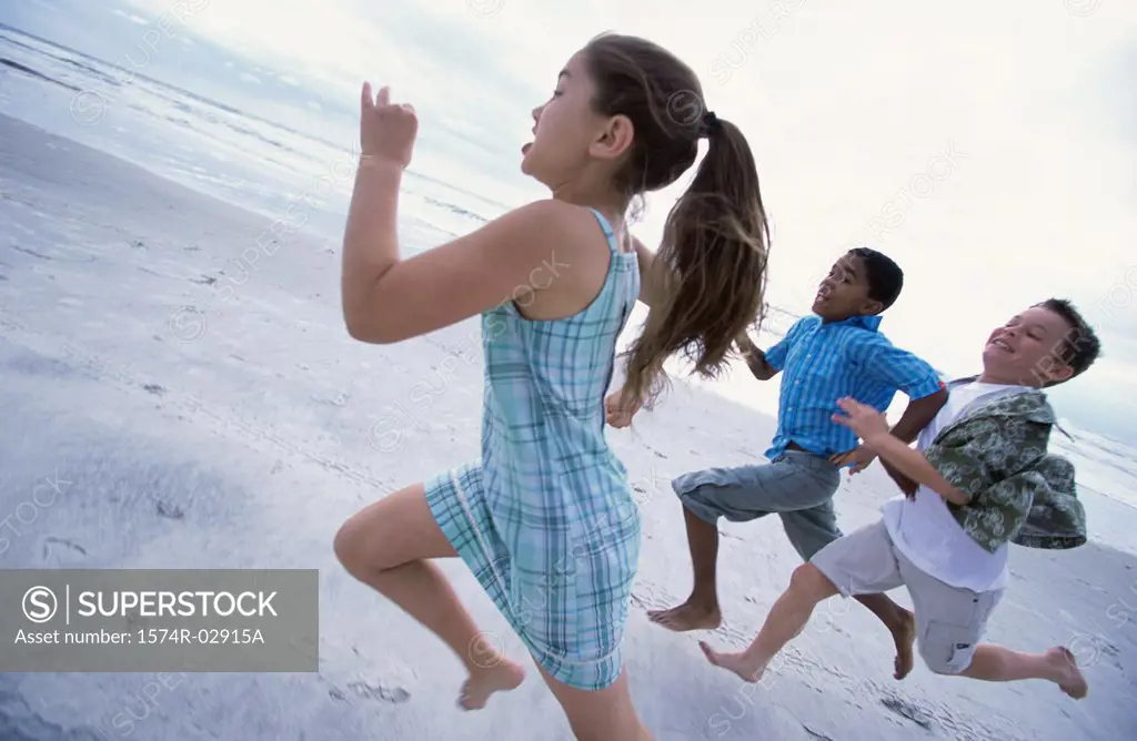Side profile of a girl and two boys running on the beach
