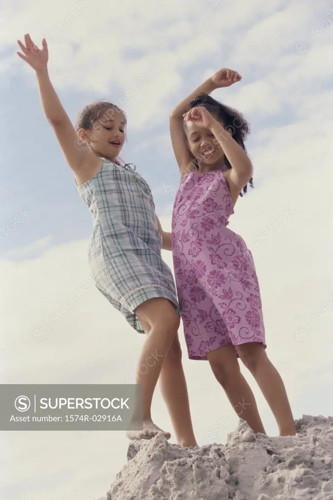Two girls standing on the beach with their arms raised