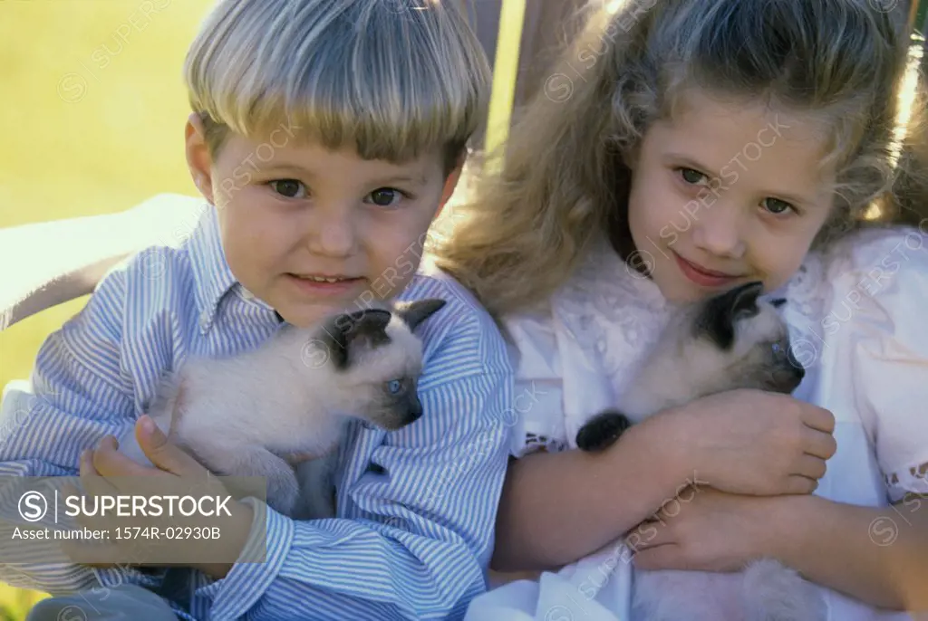 Portrait of a boy and a girl sitting with Siamese kittens