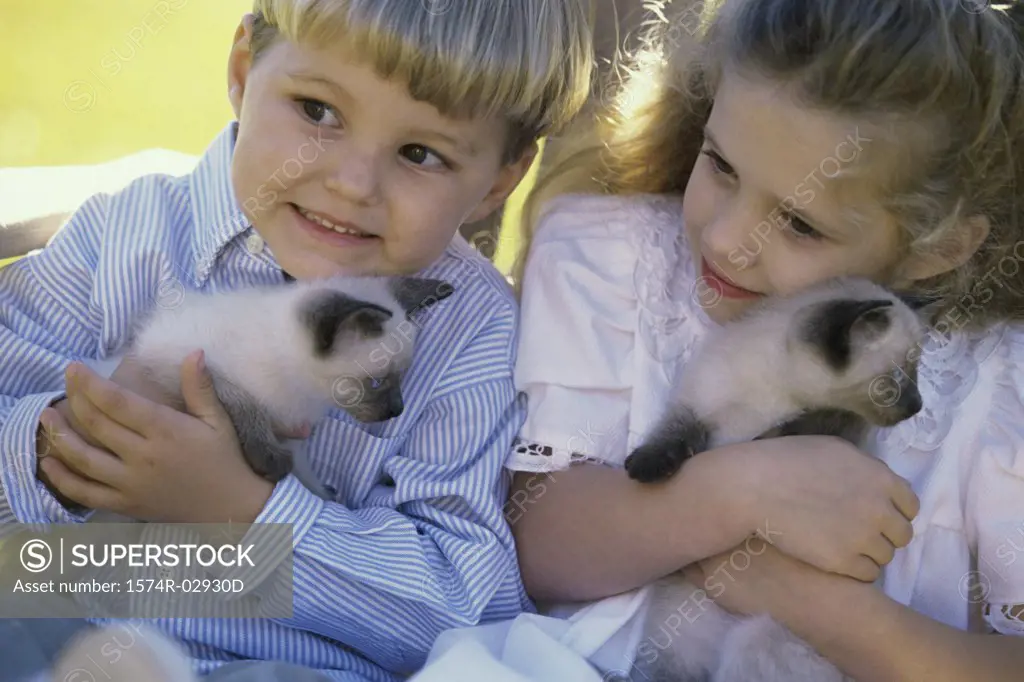 Close-up of a boy and a girl sitting with Siamese kittens